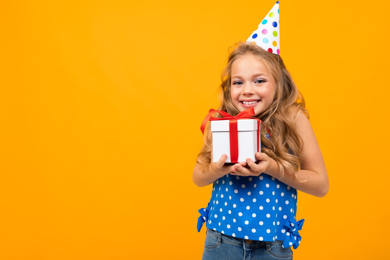 Lächelndes Mädchen mit Partyhut hält ein Geschenk vor gelbem Hintergrund – perfekte Geschenkidee für Kindergeburtstag bei TECHTRAL.