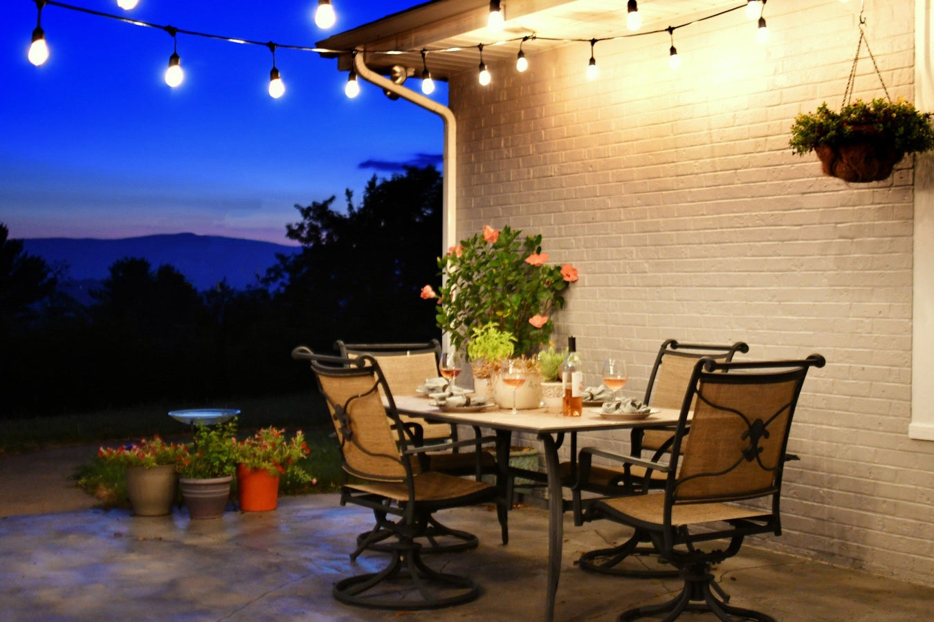 Außenbeleuchtung auf Terrasse mit LED-Lichterkette über Esstisch, gemütliche Abendstimmung im Garten.