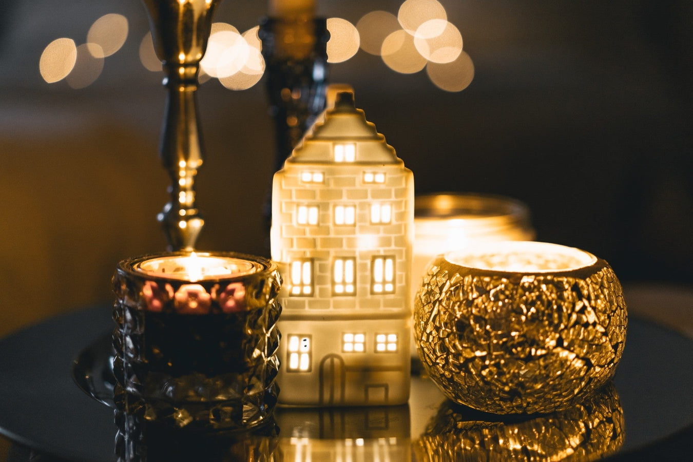 Gemütliche Dekobeleuchtung mit Kerzen und LED-Dekohaus auf einem Tisch – stilvolle Wohnatmosphäre.