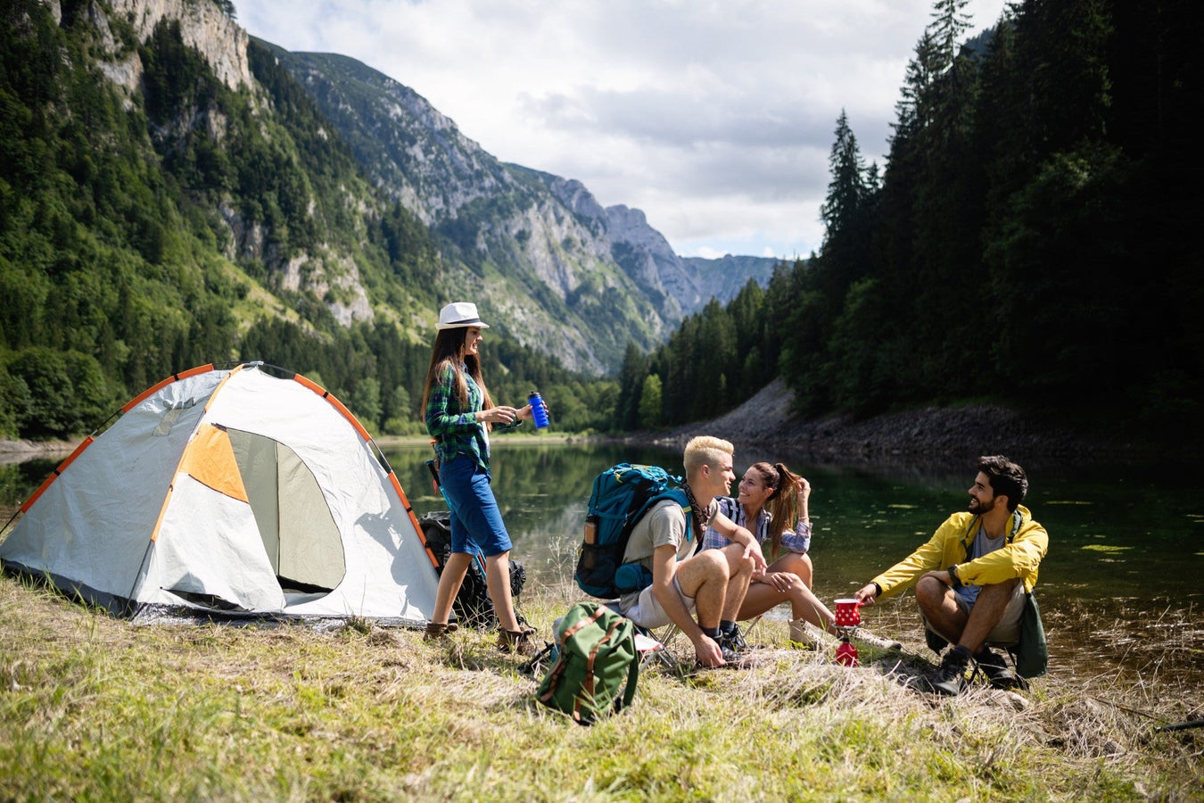 Gruppe junger Menschen beim Camping in den Bergen – mit Zelt, Rucksack und Natur im Hintergrund. Symbol für Outdoor-Abenteuer und aktive Freizeitgestaltung.