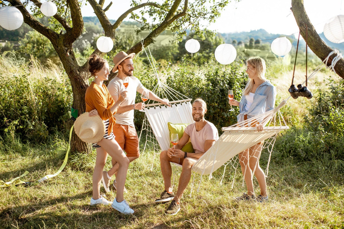 Freunde entspannen sich im Garten mit Hängematten, Getränken und Sommersonne – Outdoor-Atmosphäre in der Natur.