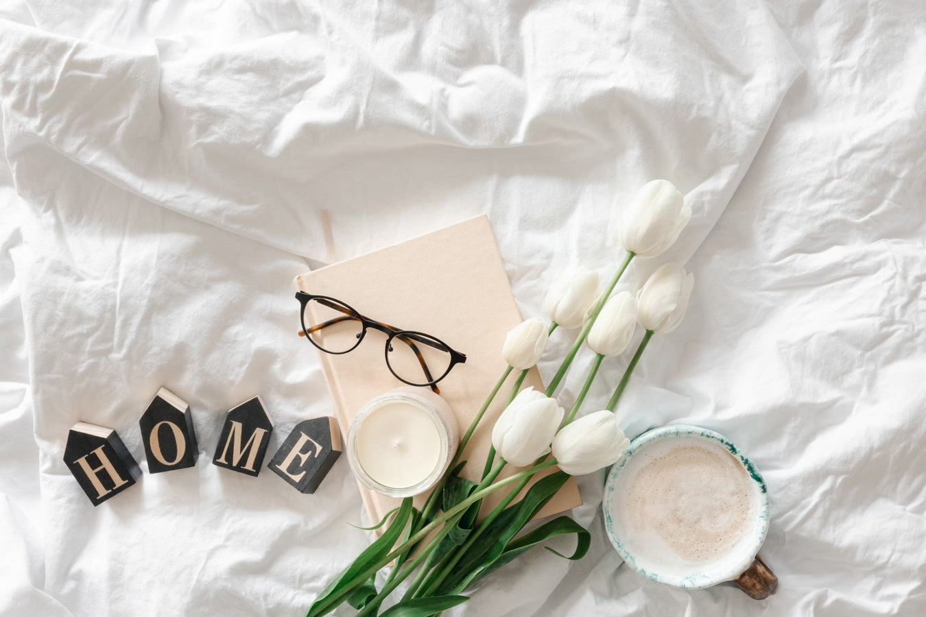 Stilvolles Stillleben mit Tulpen, Kerze und Kaffee auf weißem Bettbezug – perfekte Darstellung für moderne Wohnästhetik.