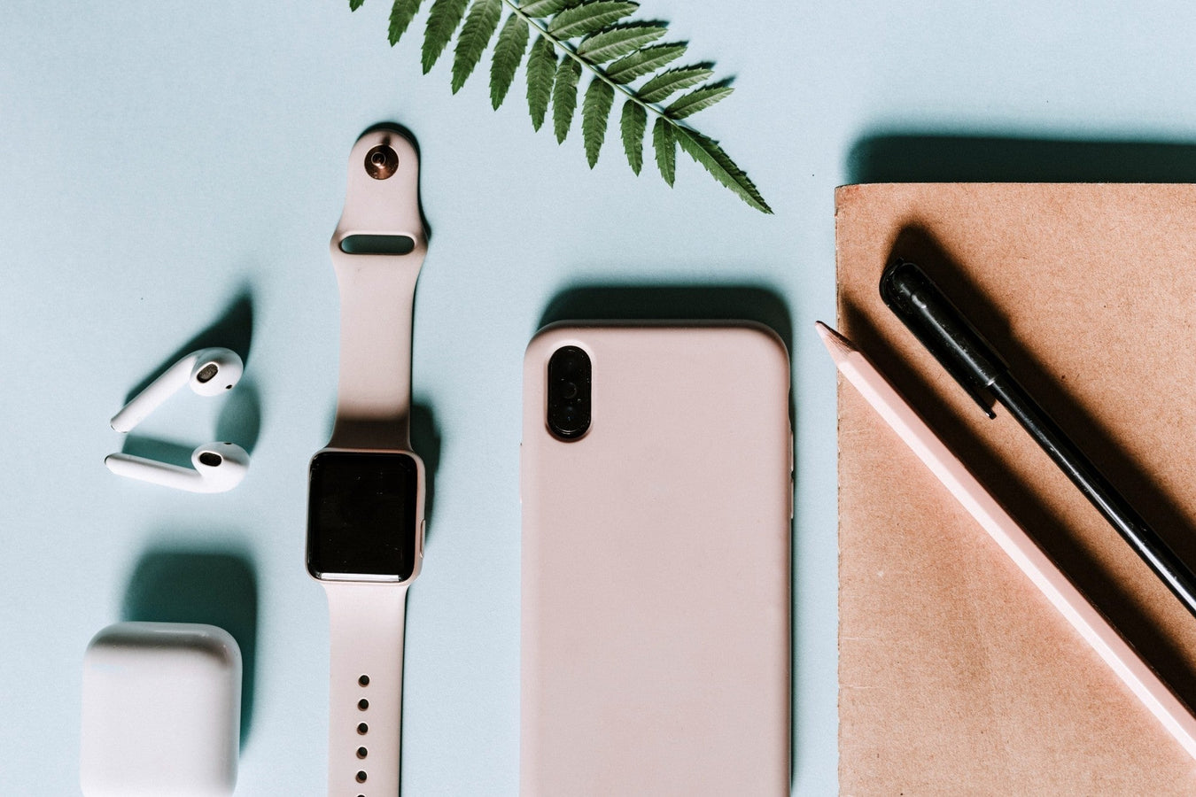 Minimalistisches Home-Office mit rosa Smartwatch, Smartphone und AirPods auf blauem Hintergrund – moderne Technik im Alltag.