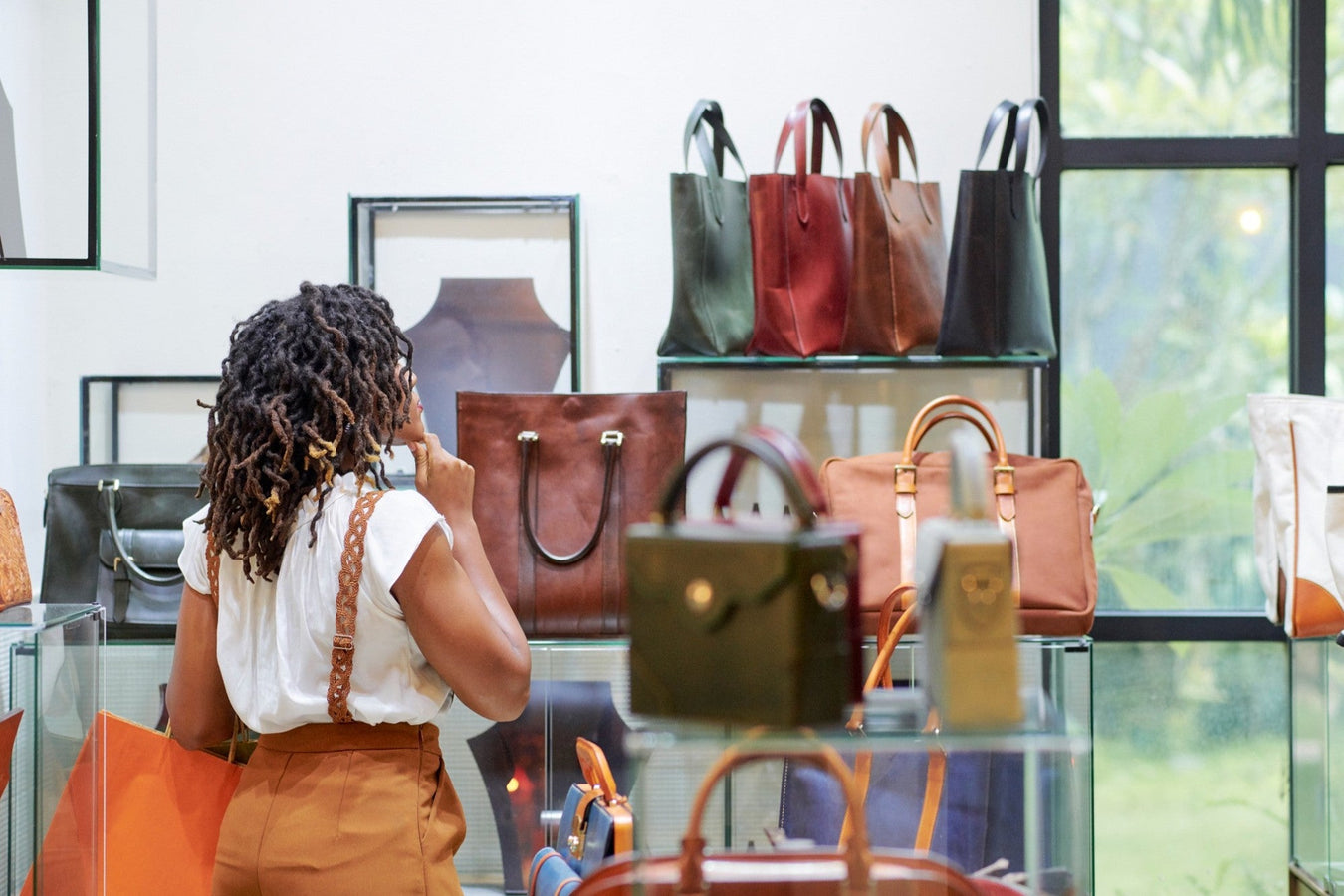 Frau kauft modische Ledertaschen und Rucksäcke in einem stilvollen Geschäft mit natürlichem Licht, hochwertige Accessoires für Alltag und Freizeit.